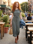 Woman in a green dress walking outdoors with tables and people in the background
