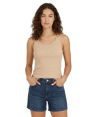Woman wearing a beige tank top and blue denim shorts on a white background