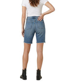 A model shown from the back wearing blue denim shorts with a raw hem, paired with a white t-shirt and black ankle boots, on a solid white background.
