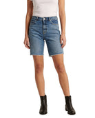 A model wearing medium-wash blue denim shorts with a raw, frayed hem, paired with a white top and black ankle boots, shown against a plain white background.